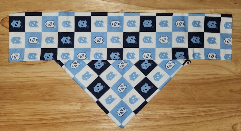 Puede incluir: Un pa&ntilde;uelo para perro a cuadros azules y blancos con un patr&oacute;n repetido de un logotipo azul y blanco. El pa&ntilde;uelo est&aacute; doblado por la mitad y est&aacute; listo para atarse alrededor del cuello de un perro.