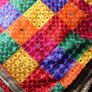 May include: A colourful fabric with a chequered pattern and embroidered flowers. The fabric has a border with silver beads and a gold trim.