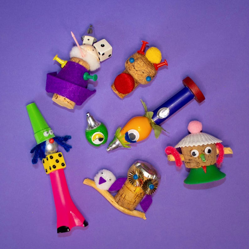Puede incluir: Una colecci&oacute;n de tapones de botella caprichosos, cada uno con un dise&ntilde;o &uacute;nico. Los tapones presentan diversos elementos como dados, pompones y figuras en miniatura, con una paleta de colores vibrantes que incluye morado, verde y rosa. El fondo es morado liso.