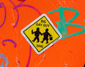 May include: A yellow warning sign with the text "BIG GAY GUY" and a silhouette of two people walking, with the text "XING" at the bottom. The sign is on an orange background with a green "B" drawn on it.