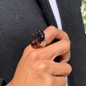 May include: A silver ring with a large, oval-shaped, dark brown gemstone. The gemstone has a faceted cut and is set in a silver band.