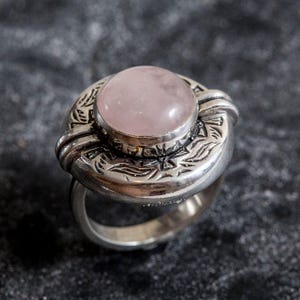 May include: A silver ring featuring a pink rose quartz stone set within an intricate floral design.