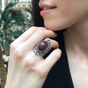 May include: A silver ring with a large, oval-shaped, reddish-brown gemstone set in a delicate, intricate design.