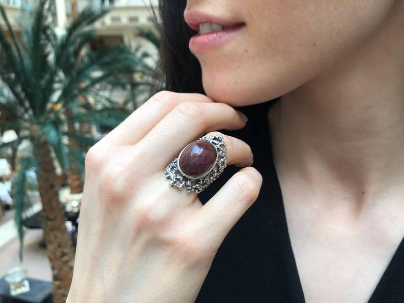 May include: A silver ring with a large, oval-shaped, reddish-brown gemstone set in a delicate, intricate design.