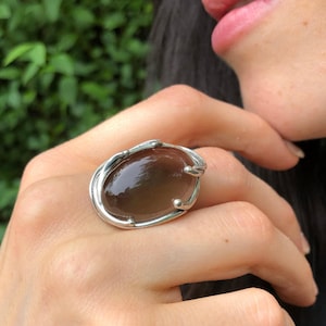 May include: A silver ring with a large, oval-shaped, dark brown gemstone set in a delicate, organic-shaped setting.