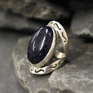 May include: A silver ring with a dark blue oval-shaped gemstone. The ring has a decorative design on the band.