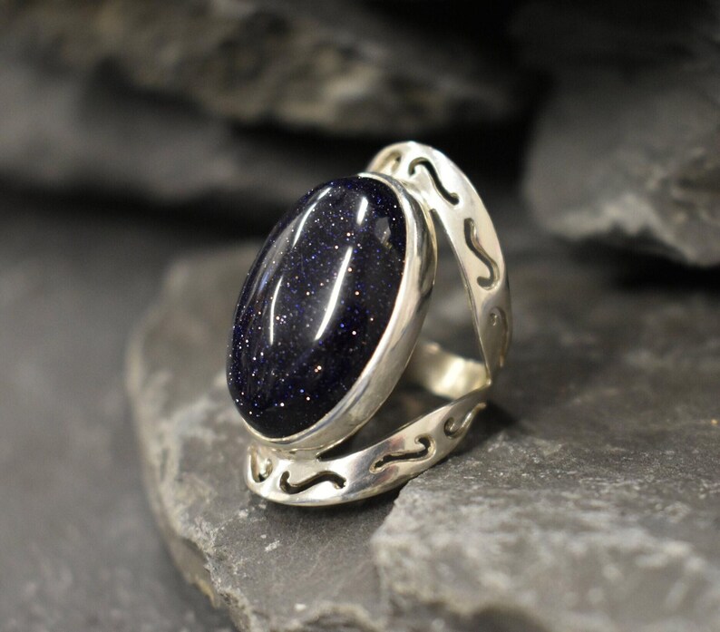 May include: A silver ring with a dark blue oval-shaped gemstone. The ring has a decorative design on the band.