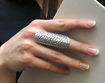 May include: A silver ring with a textured, geometric design. The ring is wide and appears to be made of metal.