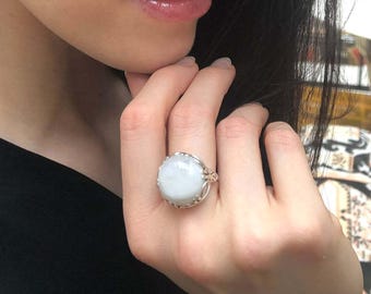 May include: A silver ring with a large, round, white gemstone set in a delicate, intricate design.