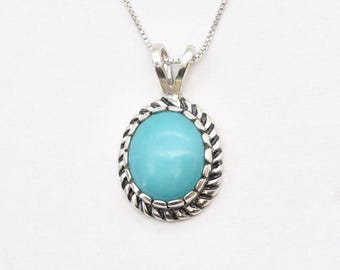 Puede incluir: Un collar de plata con un colgante de turquesa. El colgante tiene forma ovalada y un diseño de cuerda de plata alrededor del borde.