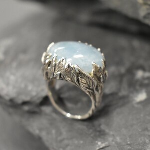 Puede incluir: Un anillo de plata con una piedra preciosa azul claro engastada en un diseño de hojas.