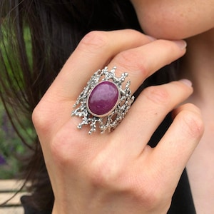Puede incluir: Un anillo de plata con una gran piedra preciosa ovalada de color p&uacute;rpura engastada en un dise&ntilde;o detallado en forma de rama.
