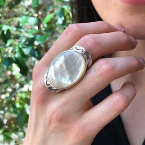 May include: A silver ring with a large oval-shaped white mother-of-pearl stone set in a delicate filigree design.