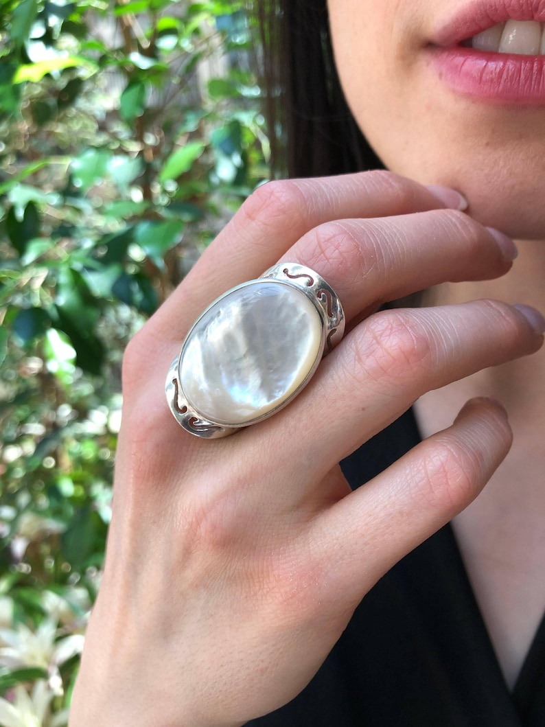 May include: A silver ring with a large oval-shaped white mother-of-pearl stone set in a delicate filigree design.