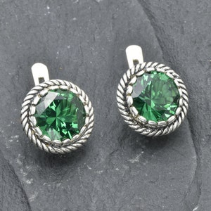 Könnte beinhalten: Ein Paar silberne Ohrclips mit einem grünen Edelstein in der Mitte jedes Ohrrings. Die Edelsteine sind von einem silbernen Seilmuster umgeben.