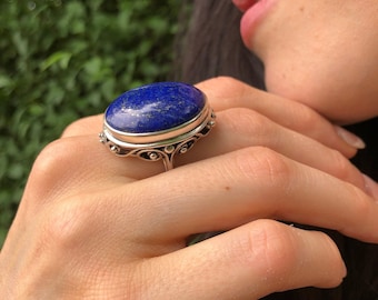 May include: A silver ring with a large oval lapis lazuli gemstone. The ring has a detailed filigree design.