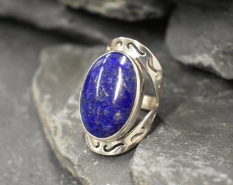 May include: A silver ring with a large oval lapis lazuli gemstone. The ring has a delicate, openwork design.