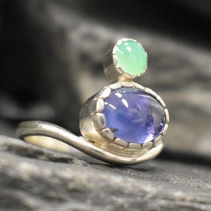 May include: A silver ring with a blue and green gemstone setting. The ring has a curved band and the gemstones are set in a bezel setting.