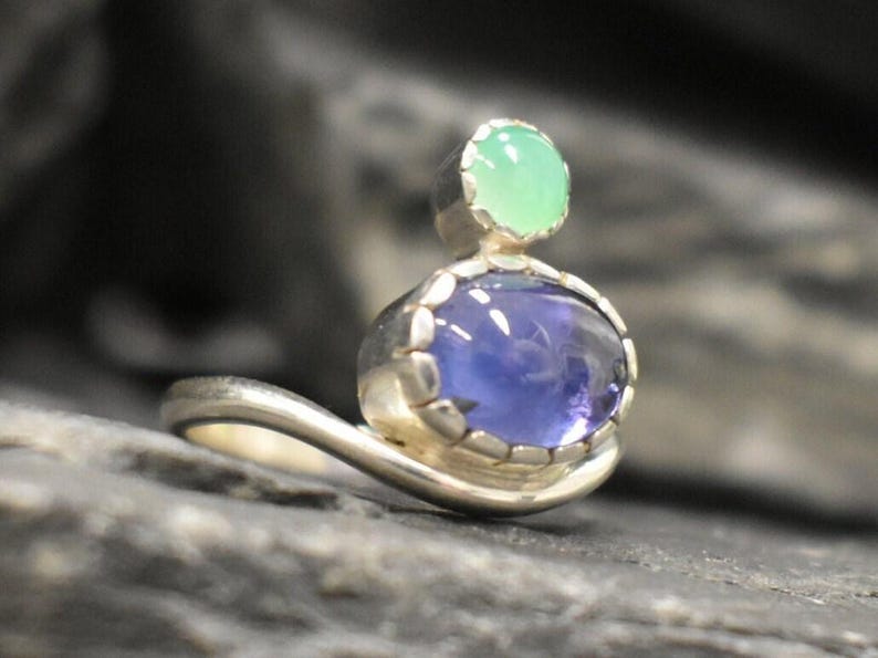 May include: A silver ring with a blue and green gemstone setting. The ring has a curved band and the gemstones are set in a bezel setting.