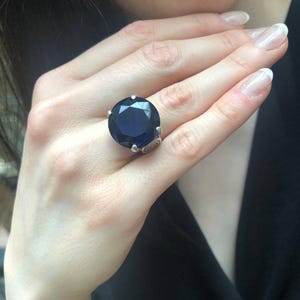 May include: A silver ring with a large, dark blue gemstone. The ring has a detailed, ornate design.