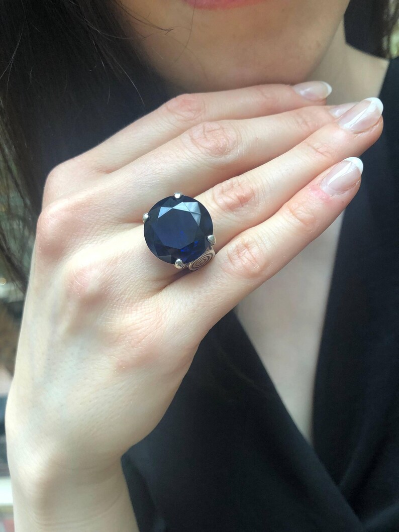 May include: A silver ring with a large, dark blue gemstone. The ring has a detailed, ornate design.
