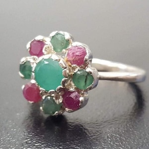 May include: A silver ring with a green gemstone surrounded by smaller pink and green gemstones.