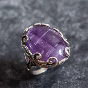 May include: A silver ring with an oval-shaped amethyst gemstone set in a decorative filigree design.