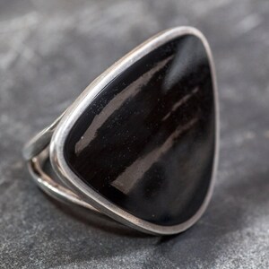 May include: A silver ring with a black triangular stone. The stone has a striated pattern.
