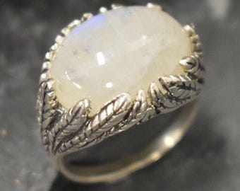 May include: A silver ring with a large, oval-shaped moonstone set in a leafy design.