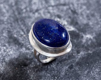 May include: A silver ring with a large oval lapis lazuli gemstone. The stone is a deep blue color with gold flecks.