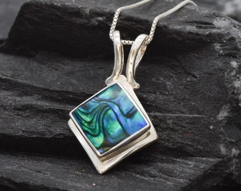 May include: A silver pendant necklace with a square abalone shell inlay. The shell has a blue, green, and iridescent color pattern.