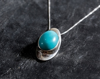 Puede incluir: Un collar de plata con un colgante de piedra ovalada turquesa engastada en un marco de plata.