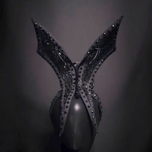 May include: A black butterfly-shaped headpiece with a black fabric base and black rhinestones. The headpiece is designed to be worn on the head.