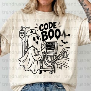 May include: A cream-colored t-shirt featuring a black graphic of a ghost wearing a nurse cap and stethoscope. The ghost stands next to an ICU monitor and IV pole. The text reads CODE BOO, accompanied by a heart rate line and small bats.