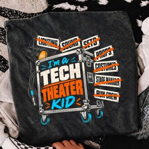 Puede incluir: Una camiseta gris oscuro con un gráfico de una caja de equipo de escenario y un foco. El texto dice I'm a TECH THEATER KID, con las etiquetas LIGHTING, SOUND, SETS, PROPS, COSTUMES, STAGE MANAGER y RUN CREW tachadas en color naranja.