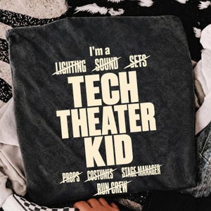 May include: A charcoal grey t-shirt featuring cream-coloured text that reads I'm a LIGHTING SOUND SETS TECH THEATER KID PROPS COSTUMES STAGE MANAGER RUN CREW, with lines striking through the specific theatre roles surrounding the main text.