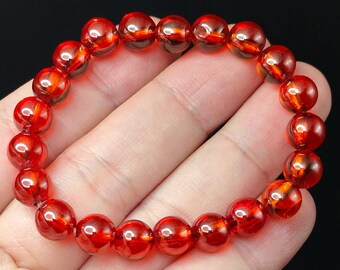 May include: A stretch bracelet composed of round, translucent, deep red beads. The beads exhibit a glossy, polished finish with subtle internal variations in color intensity, creating a vibrant, uniform appearance throughout the circular design.