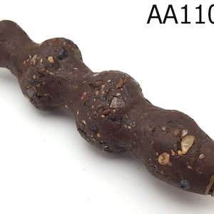 Könnte beinhalten: Ein braunes, strukturiertes, zylindrisches Objekt mit einer goldenen Kappe. Das Objekt besteht aus einem Material, das aus einer Mischung aus Ton und kleinen Steinen zu bestehen scheint.