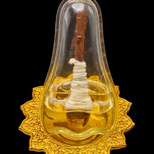 May include: A small, clear, pear-shaped container with a gold metal base. Inside the container is a brown, wooden object wrapped in white string, submerged in a clear liquid.