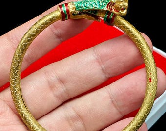Könnte beinhalten: Ein goldfarbenes Armband mit einem Drachenkopf-Design. Der Drachenkopf ist mit grünen, roten und goldenen Akzenten versehen. Das Armband hat ein Schuppenmuster. Das Armband hat einen Durchmesser von ca. 6,35 cm.
