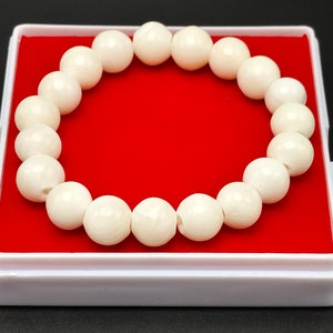 May include: A white shell bead bracelet with 18 beads, displayed in a red velvet lined box.