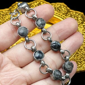 May include: A silver chain bracelet with black round beads. The beads have a rough, textured surface.