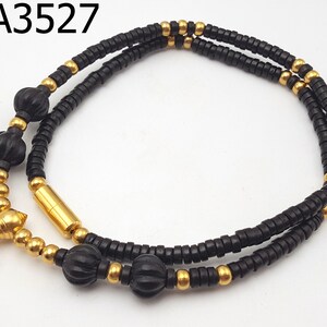 May include: A black and gold beaded necklace with a gold clasp. The necklace has a double strand of black beads and a single strand of gold beads. There are also larger black beads with a textured surface.