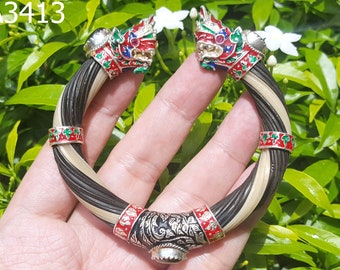 Könnte beinhalten: Ein geflochtenes Armband in Schwarz und Weiß mit silbernen und emaillierten Löwenkopf-Akzenten. Das Armband ist mit rotem und grünem Email verziert.
