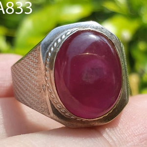 Może przedstawiać: Srebrny pierścionek z dużym, owalnym, głęboko czerwonym kamieniem szlachetnym. Pierścionek ma teksturowaną obręcz i ozdobną obwódkę wokół kamienia. Tekst "AA833" jest widoczny w lewym górnym rogu.