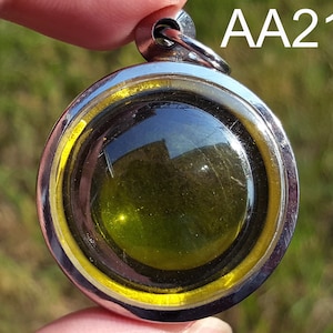 May include: A round silver pendant with a yellow border and a green glass center. The pendant has a loop at the top for attaching to a chain.