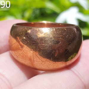 May include: A wide, gold-colored ring with an intricate design etched into the surface. The ring is worn on a finger and appears to be made of metal.