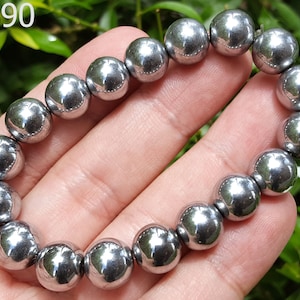 Puede incluir: Un brazalete de hematites plateado con cuentas redondas. El brazalete está hecho de 18 cuentas y tiene aproximadamente 19 cm de largo.