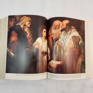 May include: An open book displays a religious illustration titled "Jesus Among the Doctors in the Temple." The artwork depicts several figures in robes, with a young boy in the center. The color palette includes browns, reds, and golds.