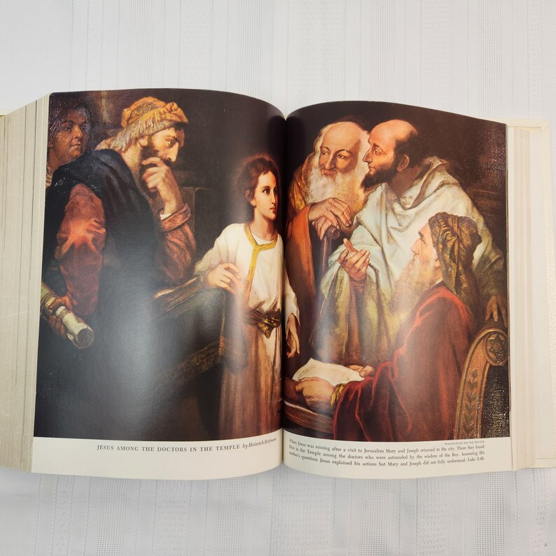 May include: An open book displays a religious illustration titled "Jesus Among the Doctors in the Temple." The artwork depicts several figures in robes, with a young boy in the center. The color palette includes browns, reds, and golds.